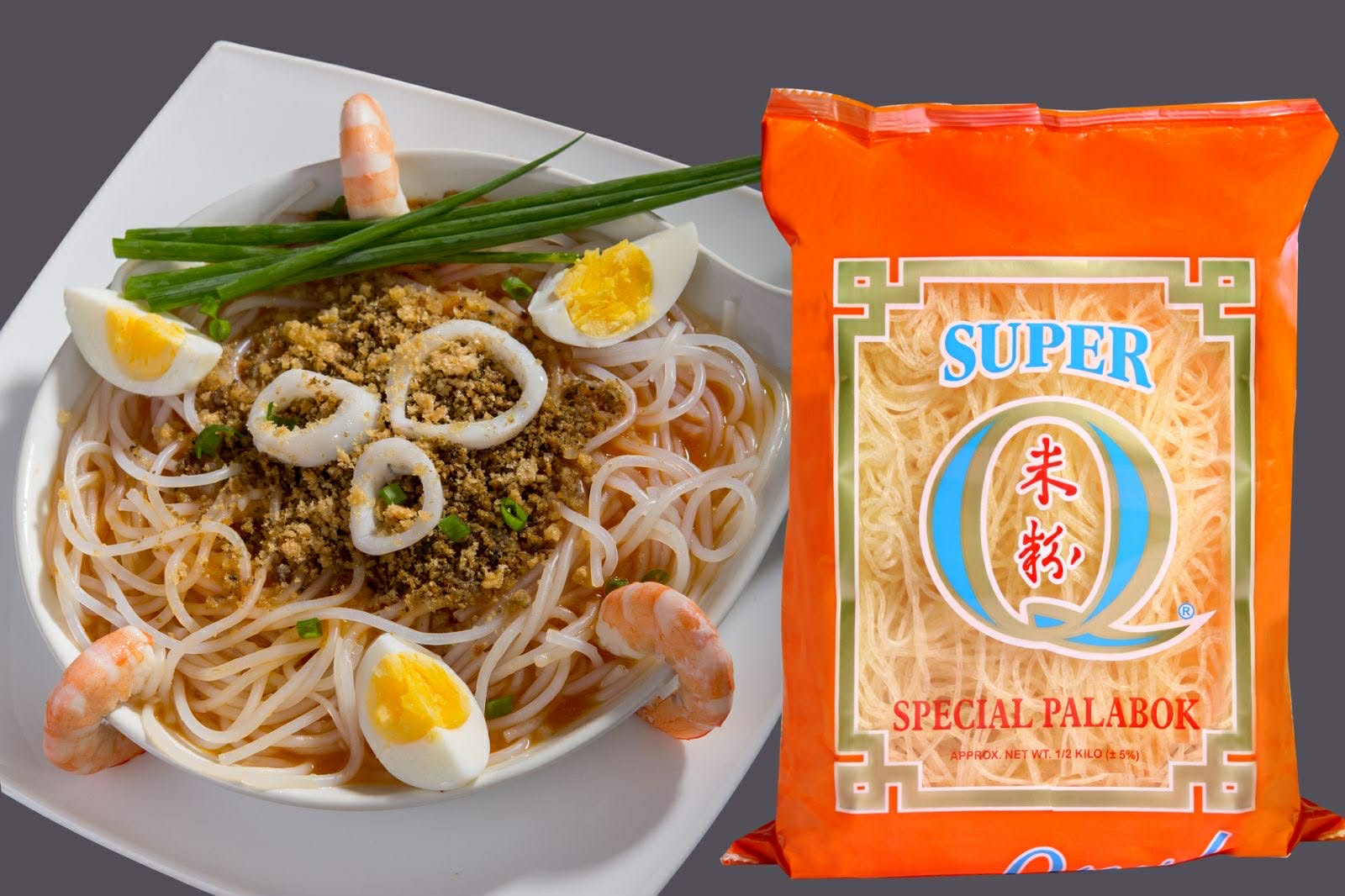 A plate of pancit palabok topped with shrimp, squid rings, boiled egg and crushed chicharon, beside a pack of Super Q Special Palabok
